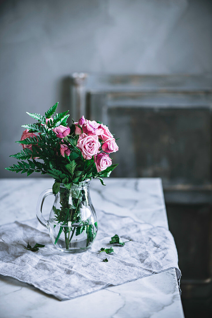 Ein Strauss rosafarbene Rosen in Glaskrug auf Tisch