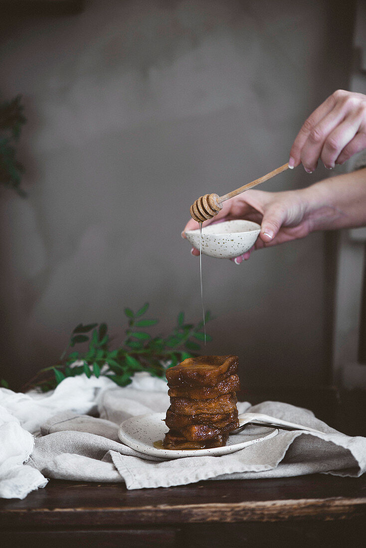 Hands of person pouring honey on chocolate dessert with wooden spoon