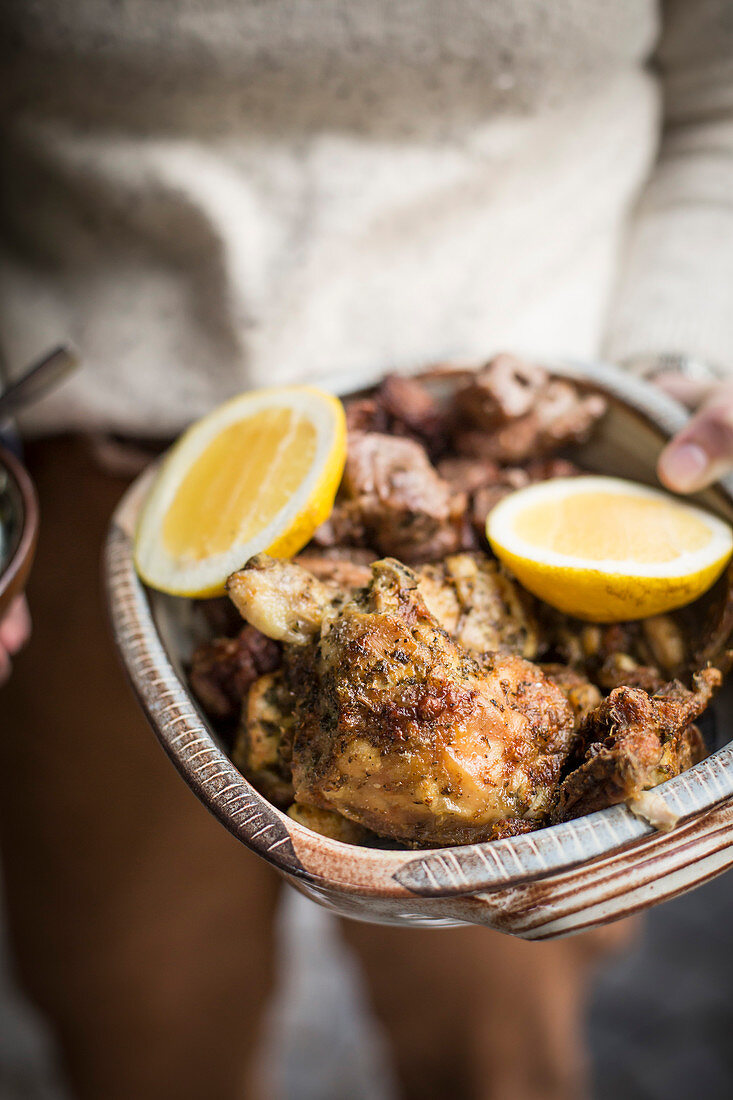 A person holding a bowl of grilled chicken and lemons