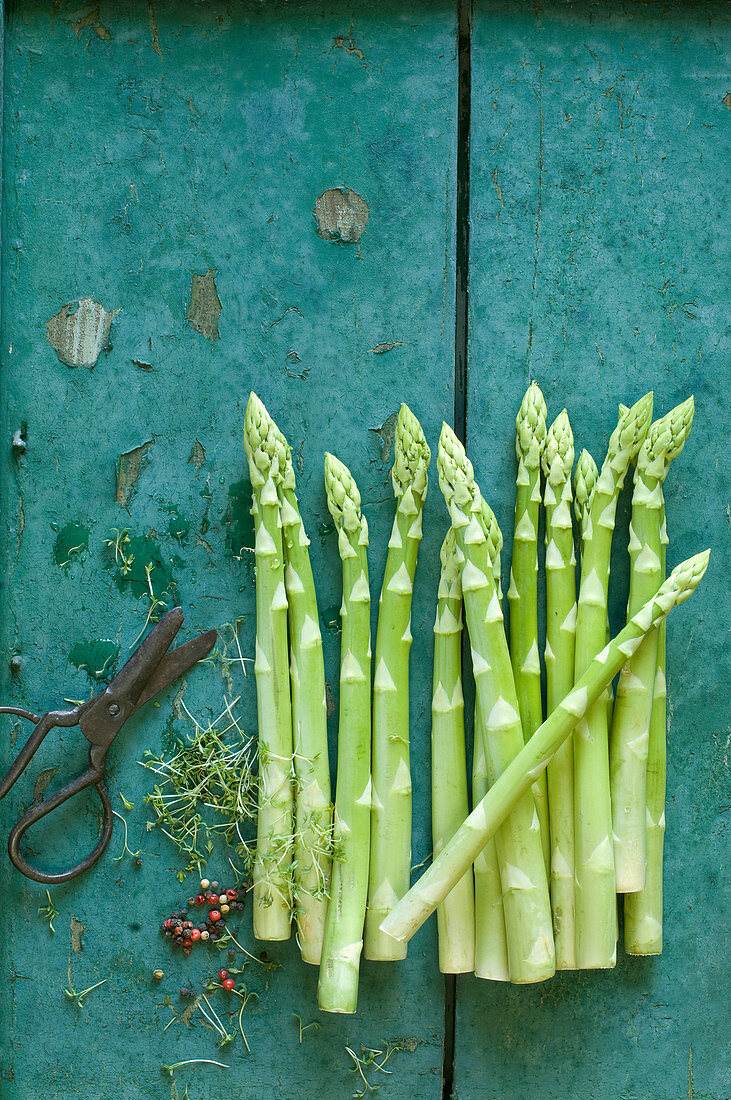 Green asparagus on a rustic wooden background with cress, peppercorns and scissors