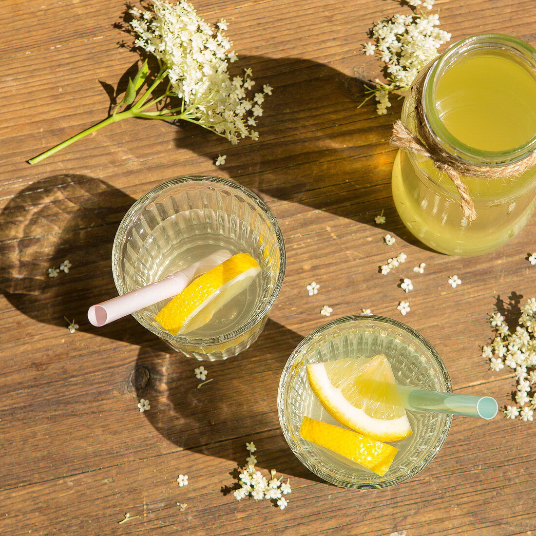 Two glasses od mixed elderflower cordial and a jar of fresh cordial on a wooden table with freshly picked Elderflowers