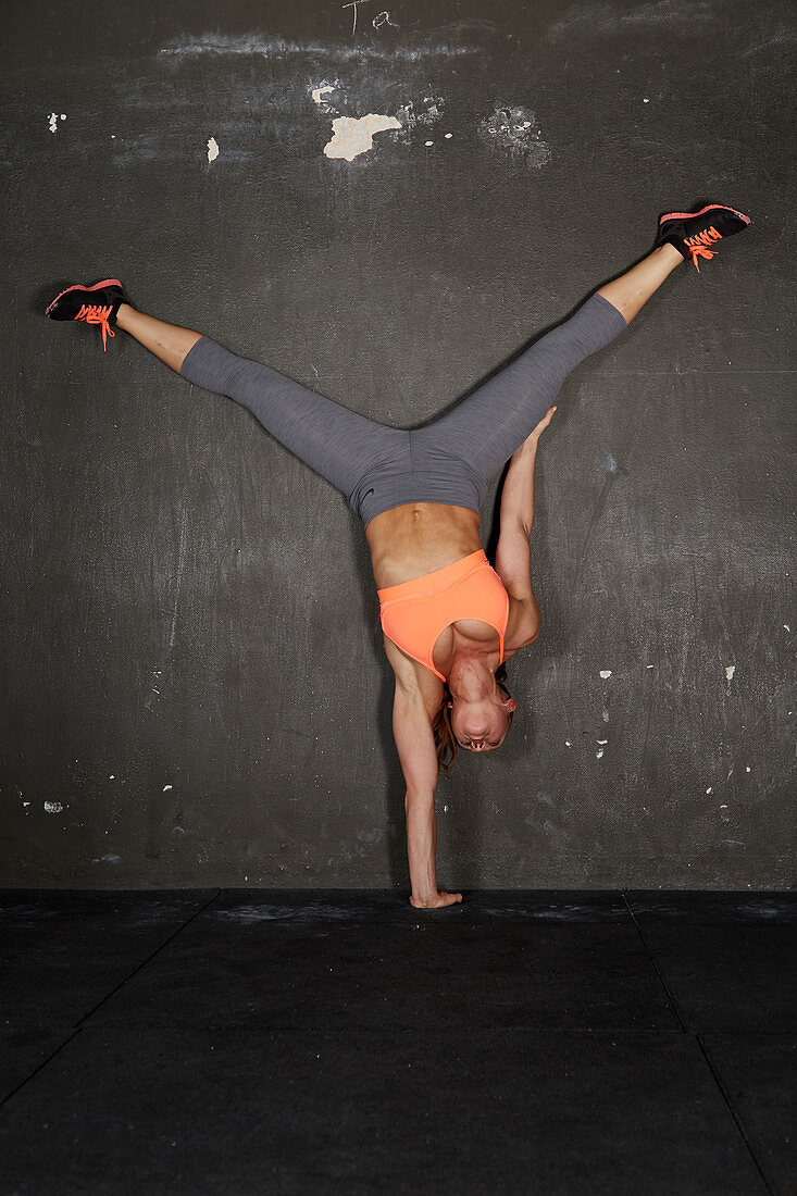 A young woman performing a one-handed wall handstand