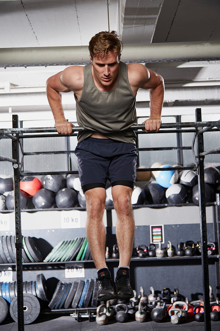 Junger Mann bei Fitnessübung Bar Muscle-Up an der Klimmzugstange