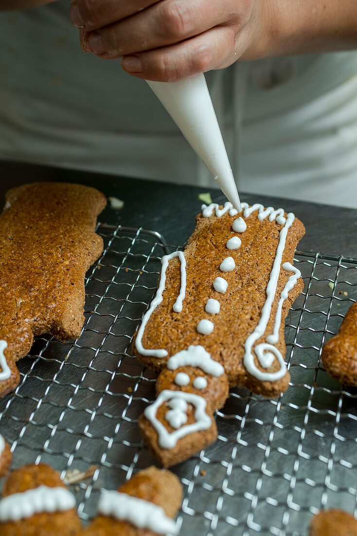 A baker decorating gingerbread men with icing from a piping bag