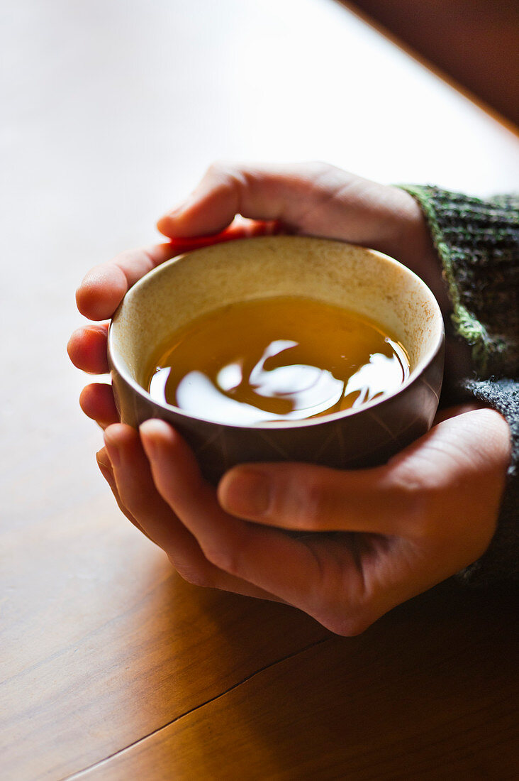 Hands holding a bowl of green tea