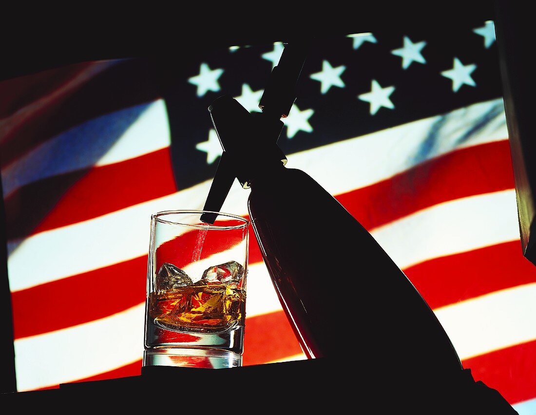 Glas Whiskey-Soda mit sprühender Sodaflasche vor USA-Flagge