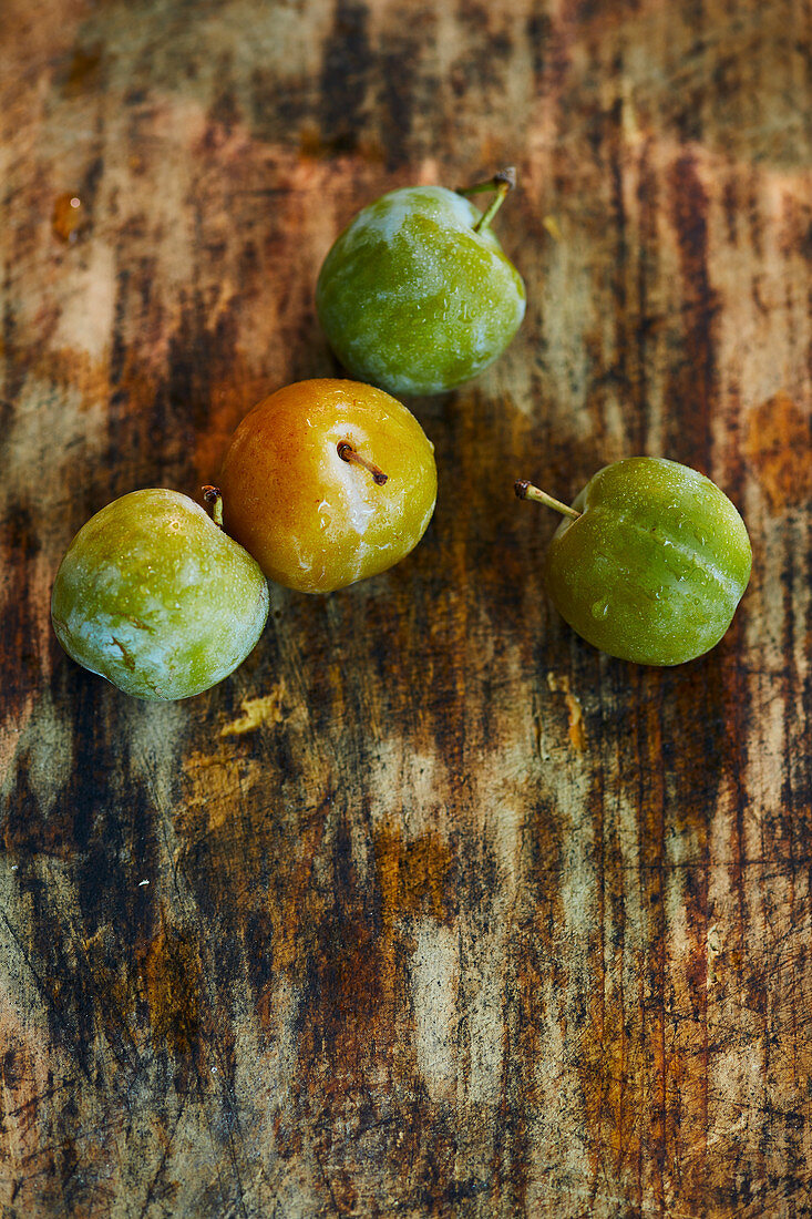Four greengages on a wooden surface