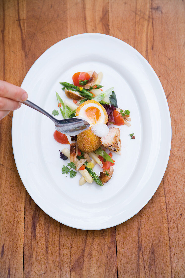 A baked egg on asparagus and tomato salad