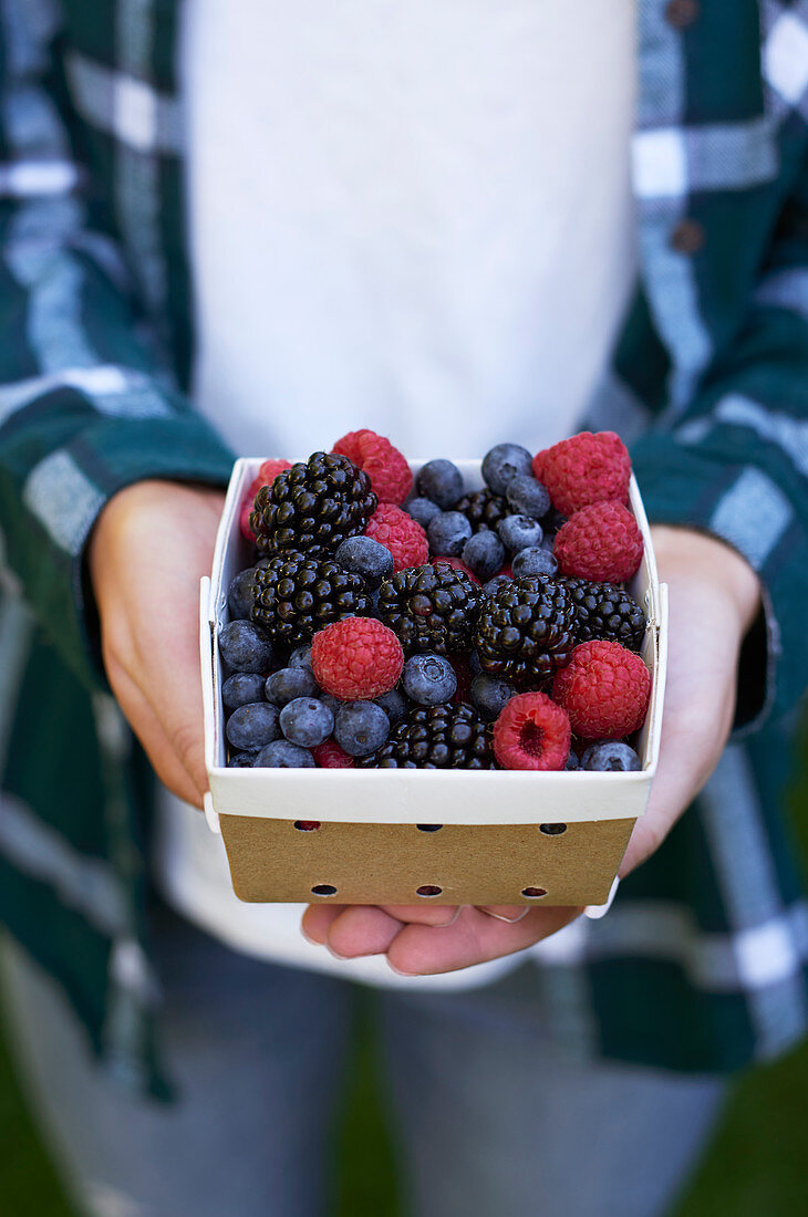 A person holding a cardboard punnet of fresh berries