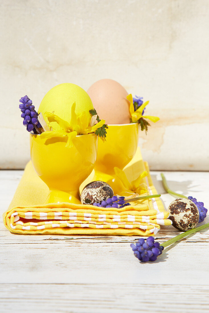 Gelbe Eierbecher österlich dekoriert mit Forsythien- und Hyazinthenblüten