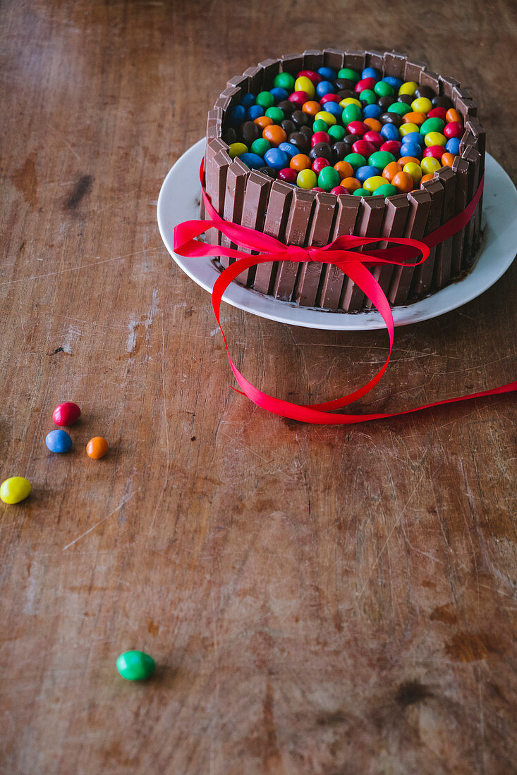 A chocolate cake with chocolate bars on a wooden table with a red ribbon for Mother's Day
