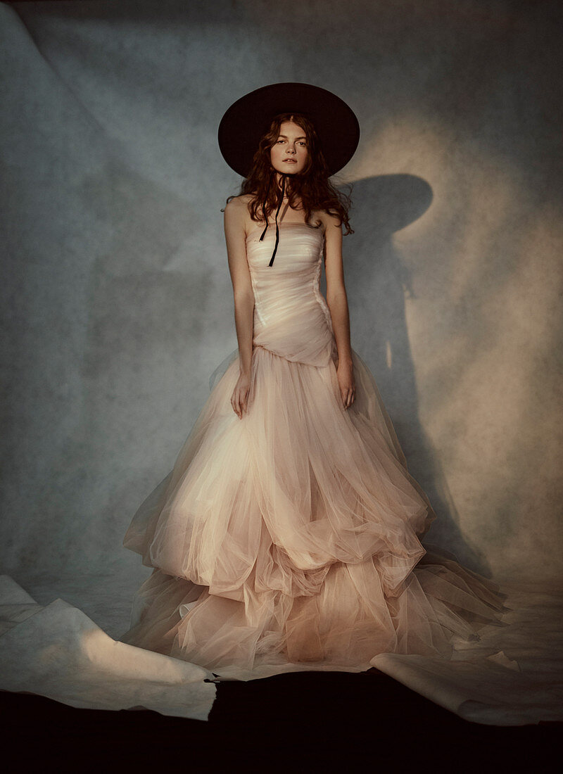 A young woman wearing a black hat, a peach dress with a ruffles top and a double frilled tulle skirt