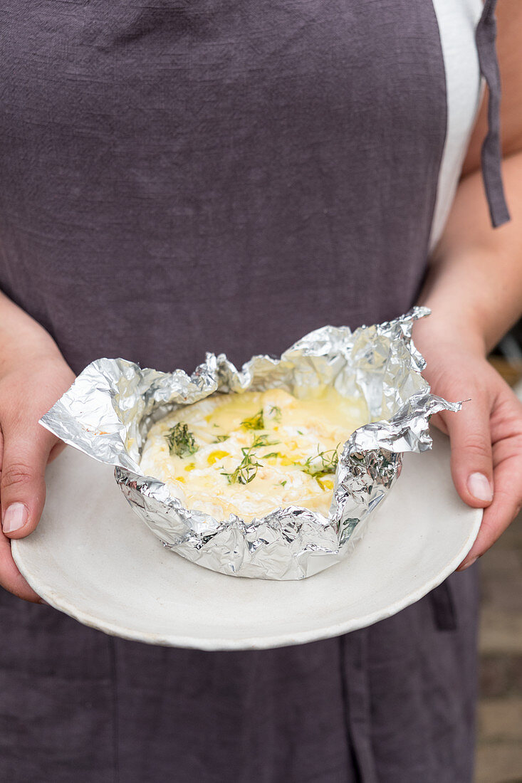 Grilled cambembert from the bbq in hands in aluminum foil with garlic and rosemary