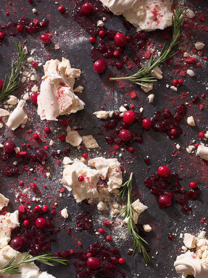 Crumbled meringue surrounded by squashed berries and rosemary sprigs
