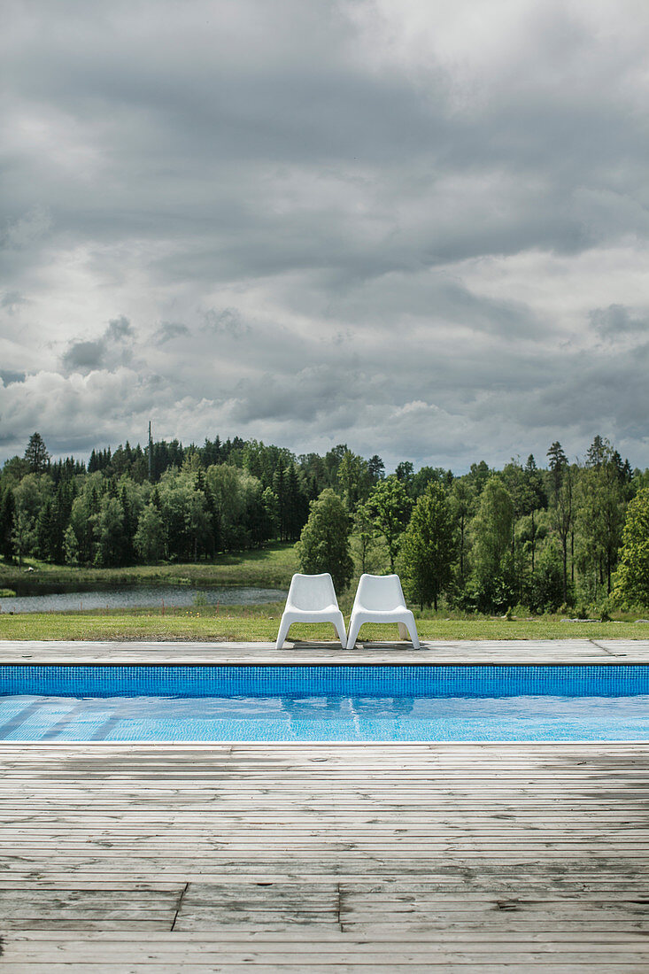 Zwei Plastikstühle am Swimmingpool mit Blick auf den Wald
