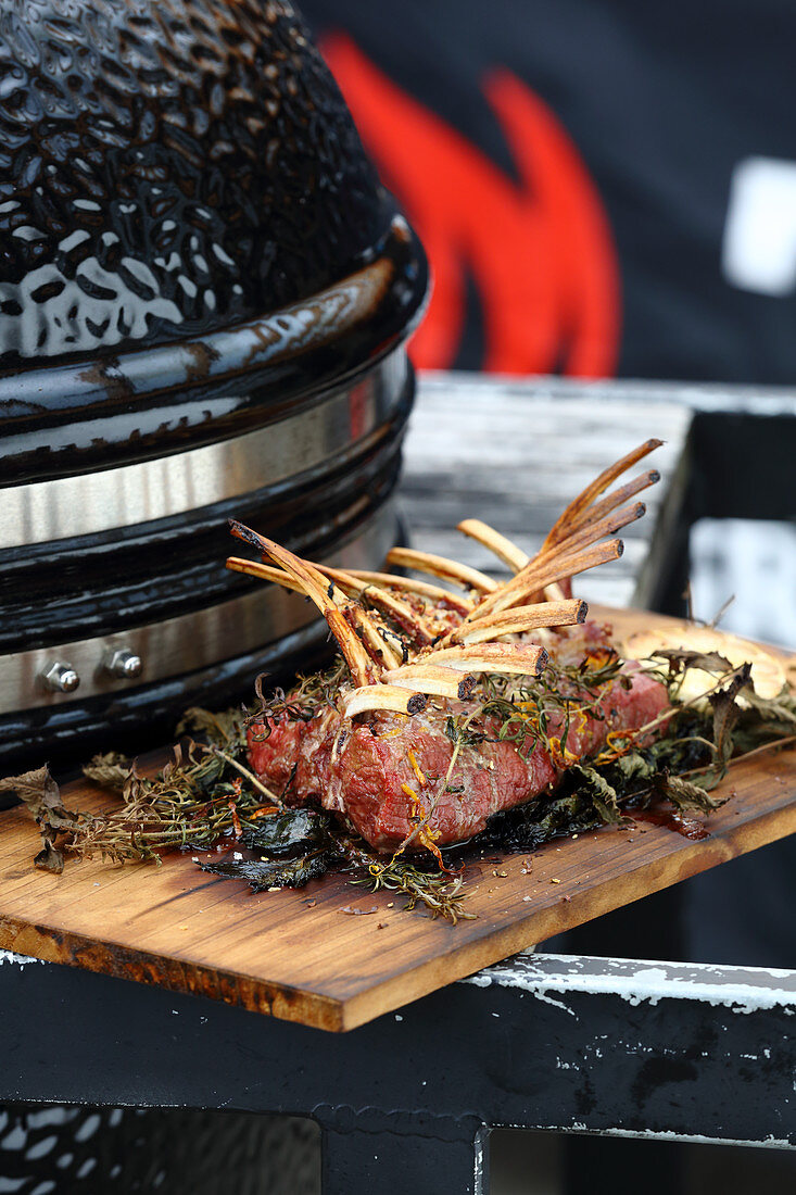 Grilled rack of lamb with herbs next to a kettle barbecue