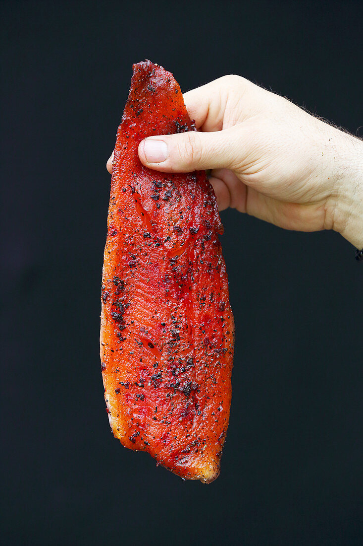 A hand holding a marinated, smoked salmon trout fillet