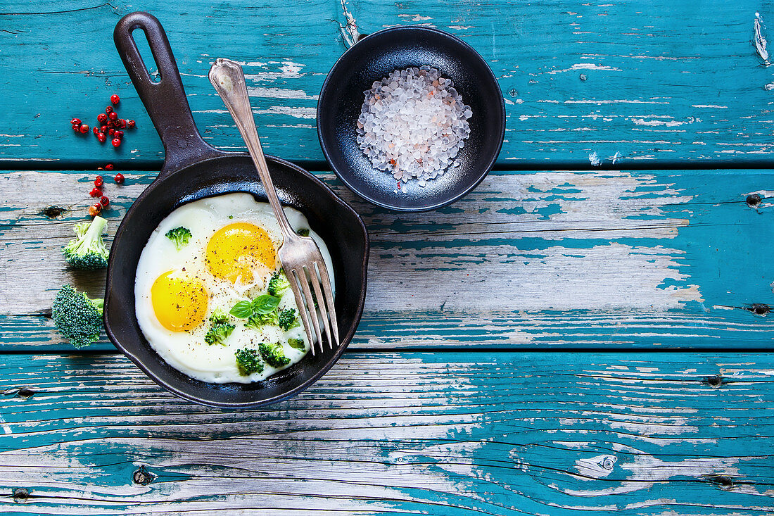 Healthy breakfast with fried eggs and green organic broccoli in old cast iron pan