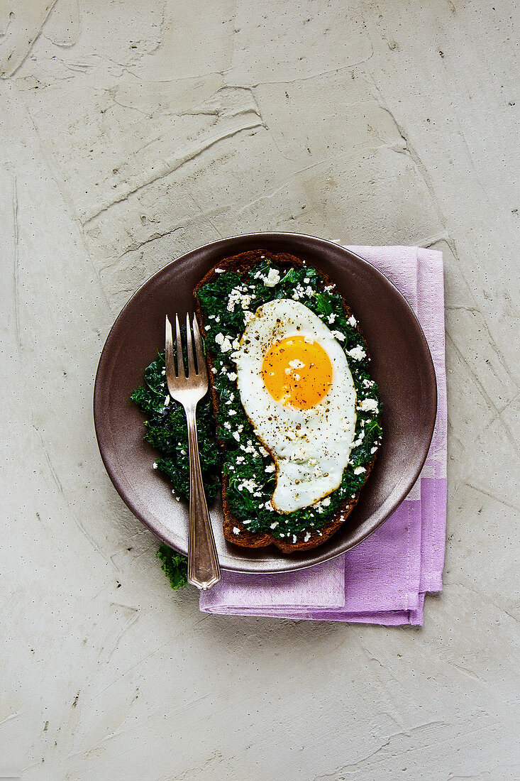 Fried egg sandwich with rye bread, kale and feta cheese on concrete background