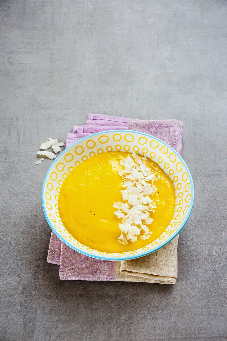 Bowl of yellow colorful mango smoothie with coconut chips