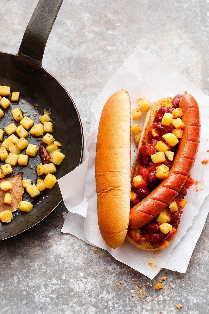 A hot dog with chili beans and potato cubes