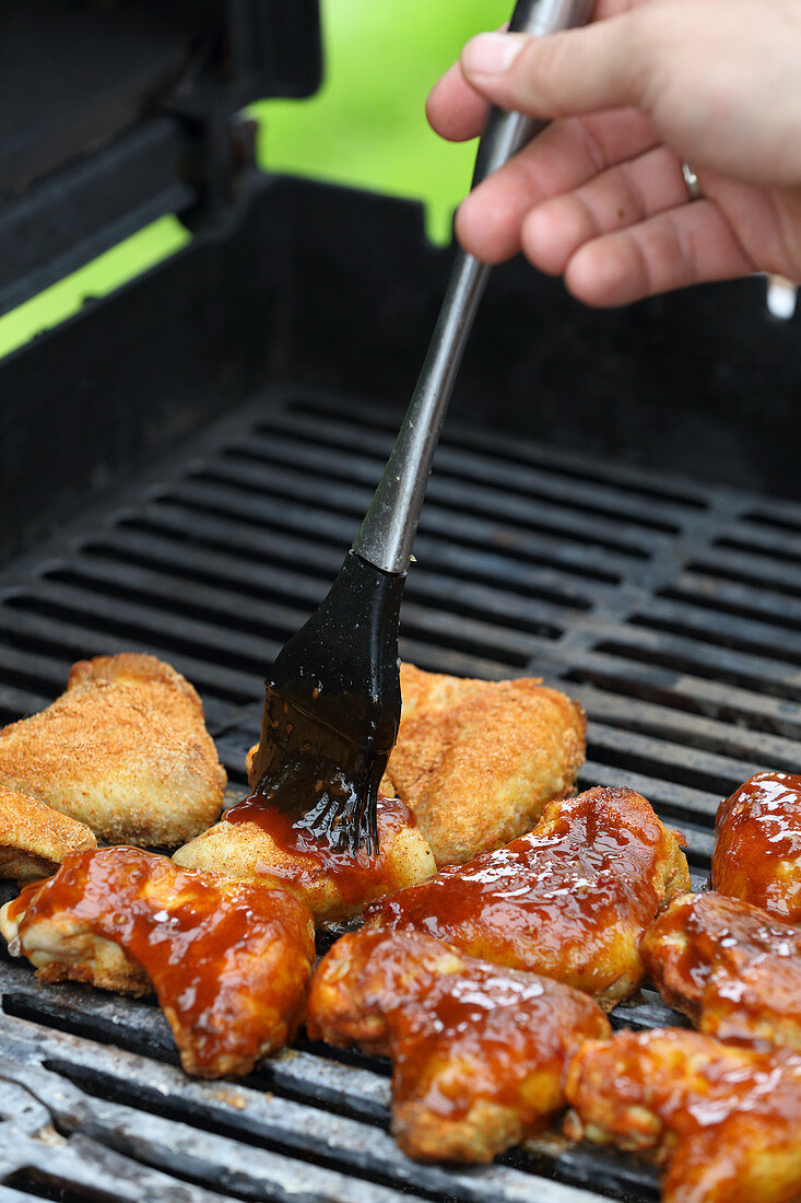 Chicken wings on a grill brushed with marinade