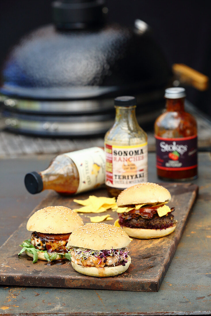 Three grilled burgers with sauces on a wooden board