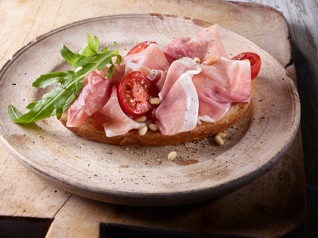A slice of bread topped with Tuscan ham, tomatoes and rocket