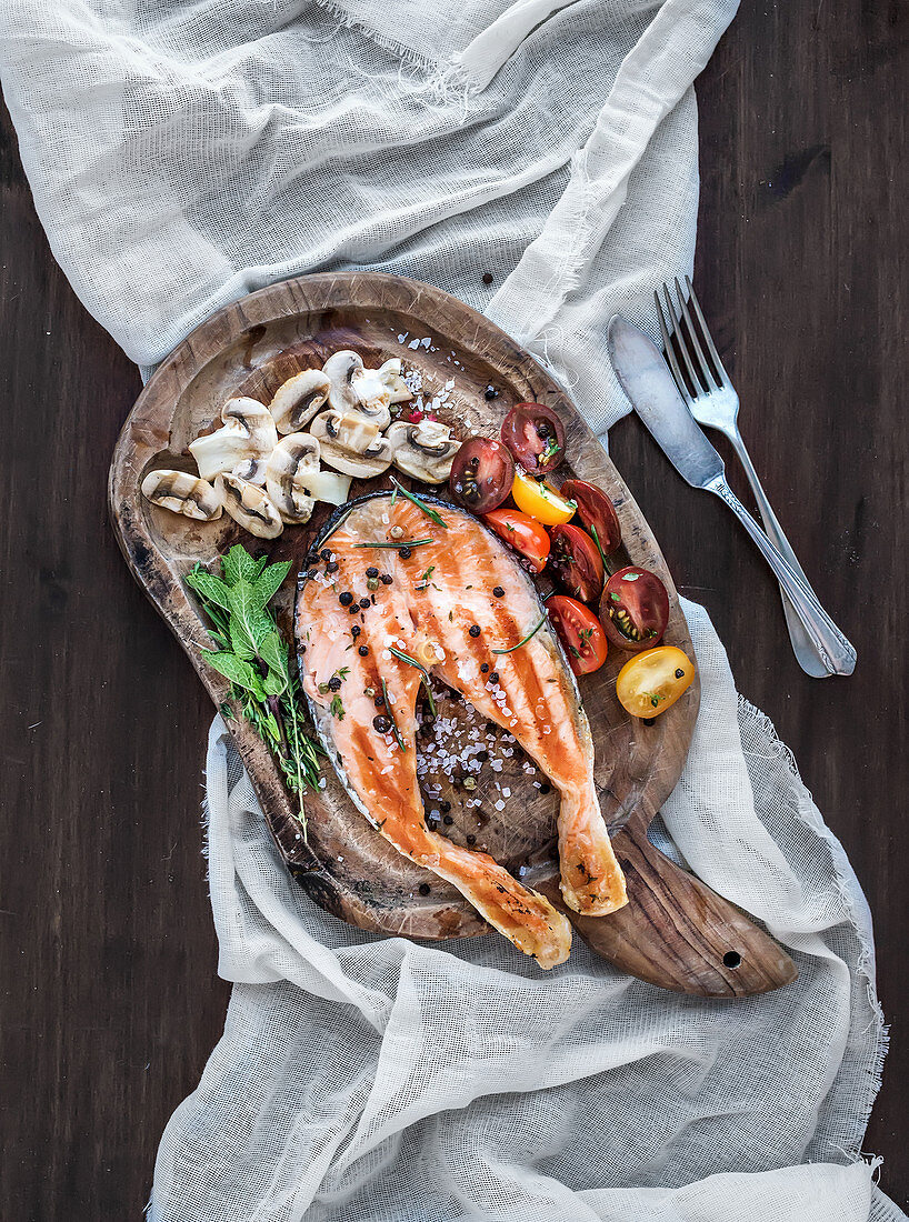 Grilled salmon steak with fresh herbs, roasted mushrooms, cherry-tomatoes and spices