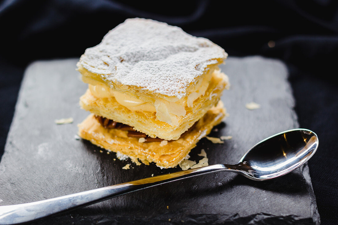 Close up of served dessert made of puff pastry and various creams topped with sugar powder