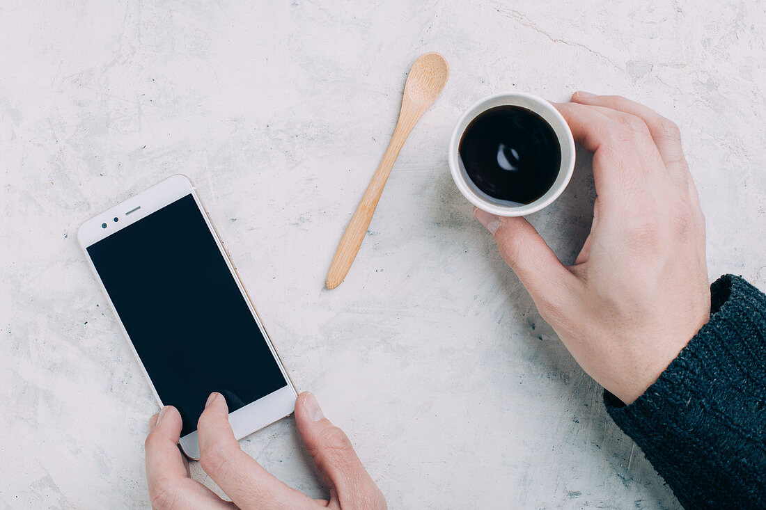 Man holding a black coffee in a disposable cup and a smartphone