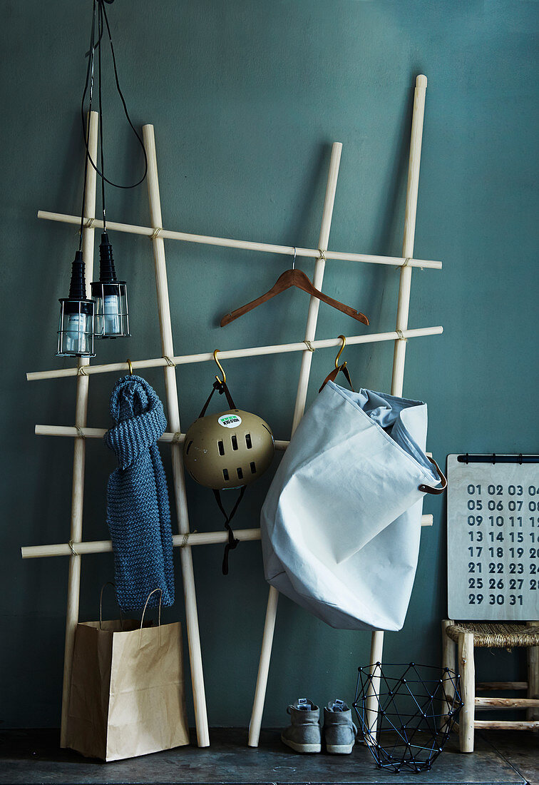 DIY-Garderobe aus Holzstäben und Fleischerhaken vor grau-grüner Wand