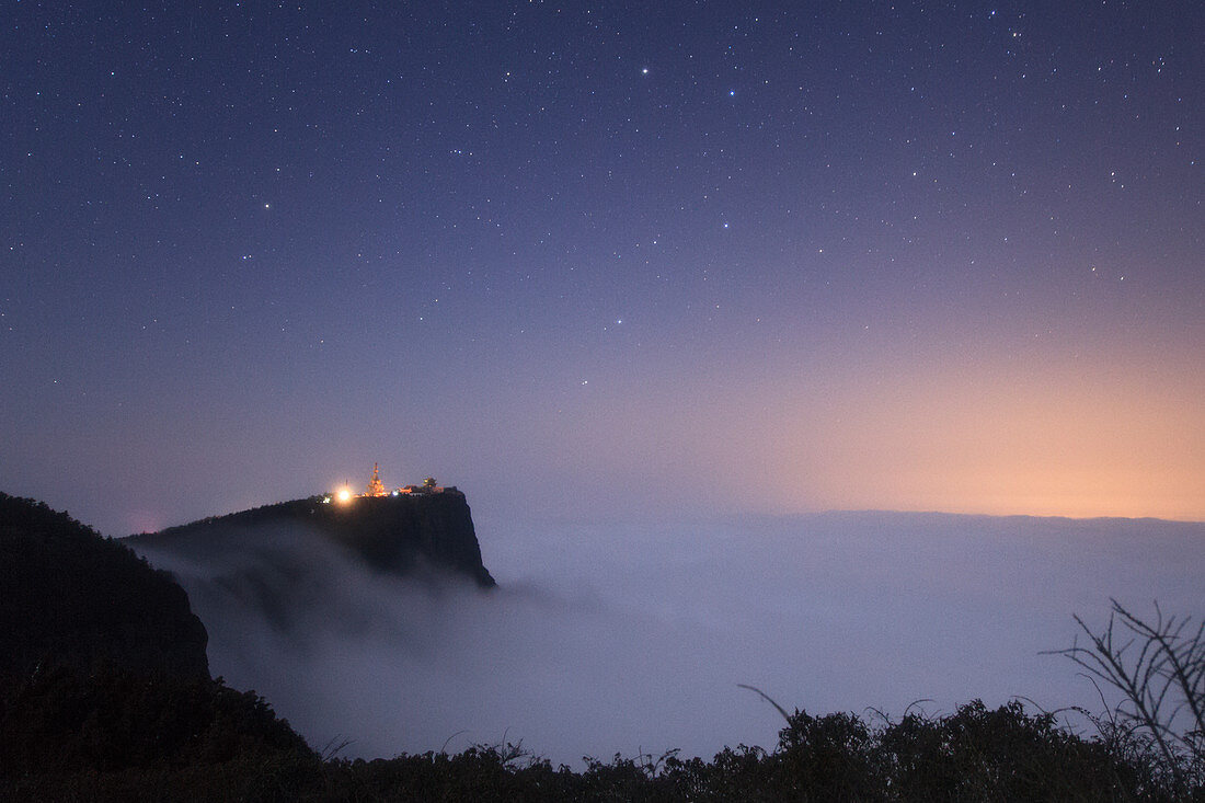 Night sky above clouds and Buddhist mountain