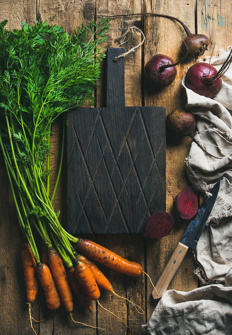 Fresh garden carrots and beetroots on rustic wooden background with dark cutting board