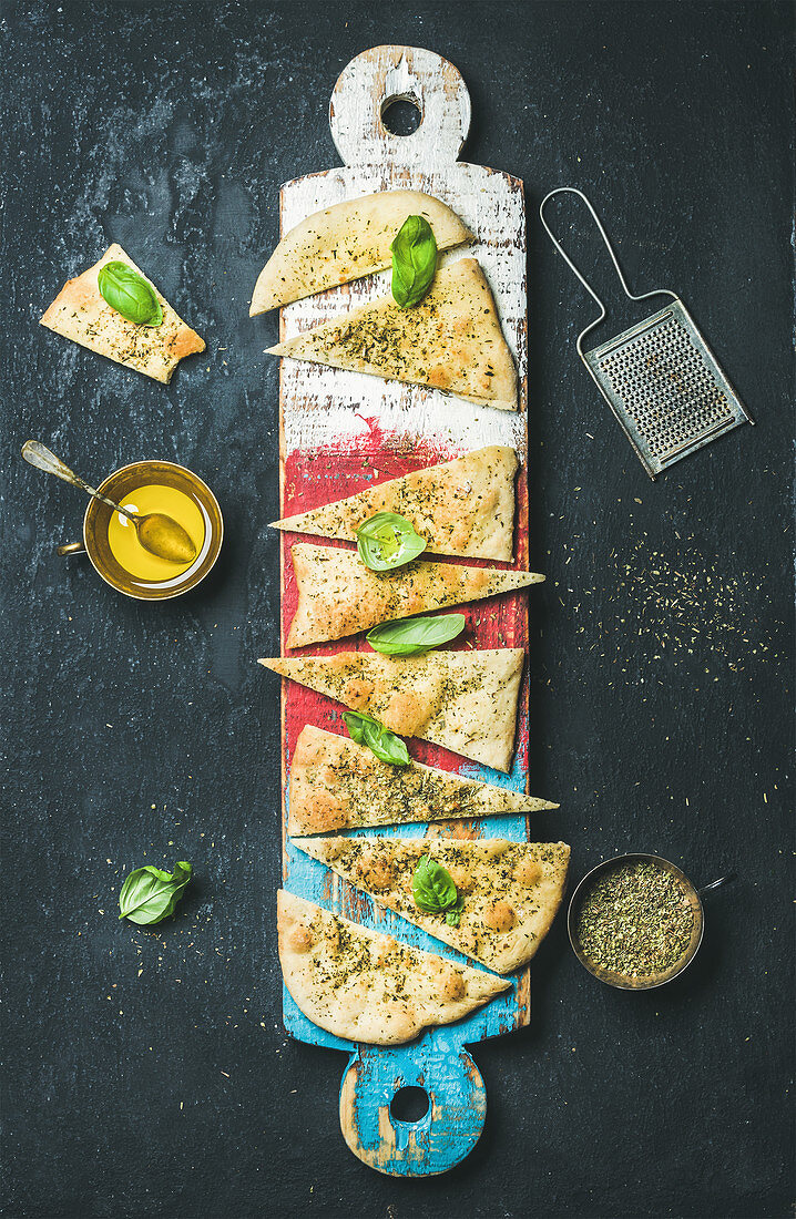 Homemade Italian focaccia flatbread cut into pieces with herbs, fresh basil leaves, olive oil and glass of rose wine