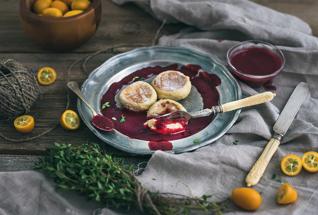 Russian cheese cakes on a vintage metal plate with lingonberry jam, fresh kumquats and thyme