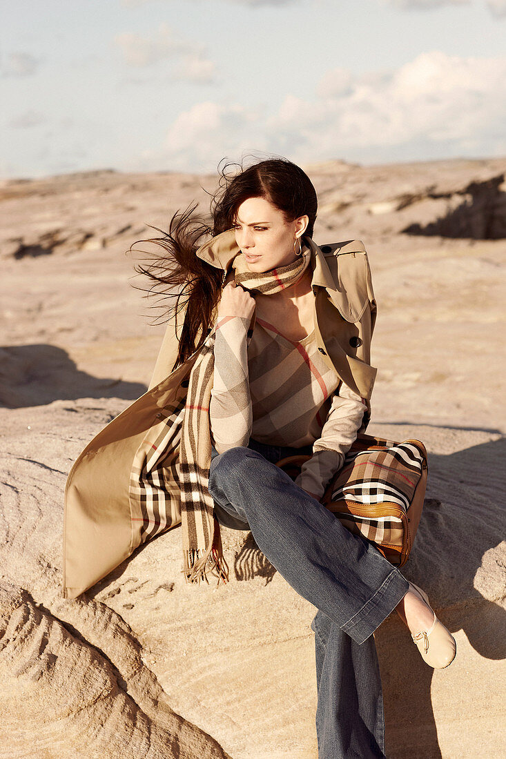 A brunette woman wearing a sand-coloured trench coat and jeans