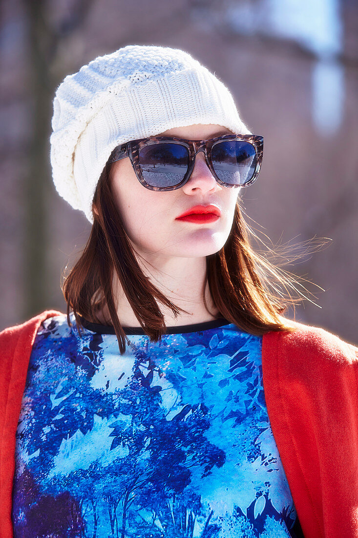 Brünette Frau mit weißer Mütze und Sonnebrille in rotem Cape und blauem Shirt