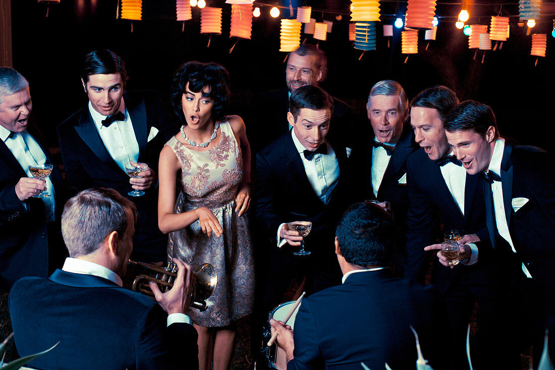 An elegantly dressed woman wearing a 1950s outfit with men at an outdoor event with a band