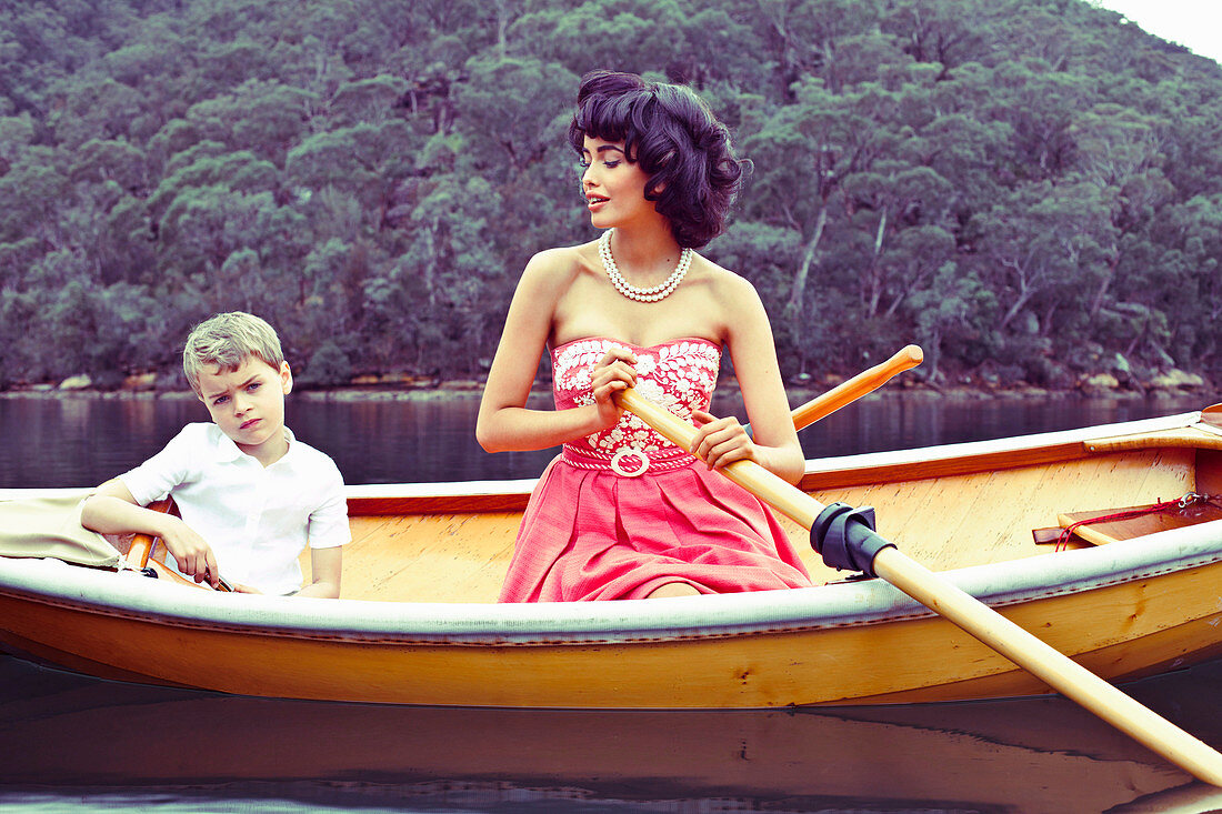 A dark-haired woman wearing a pink dress with a boy in a boat
