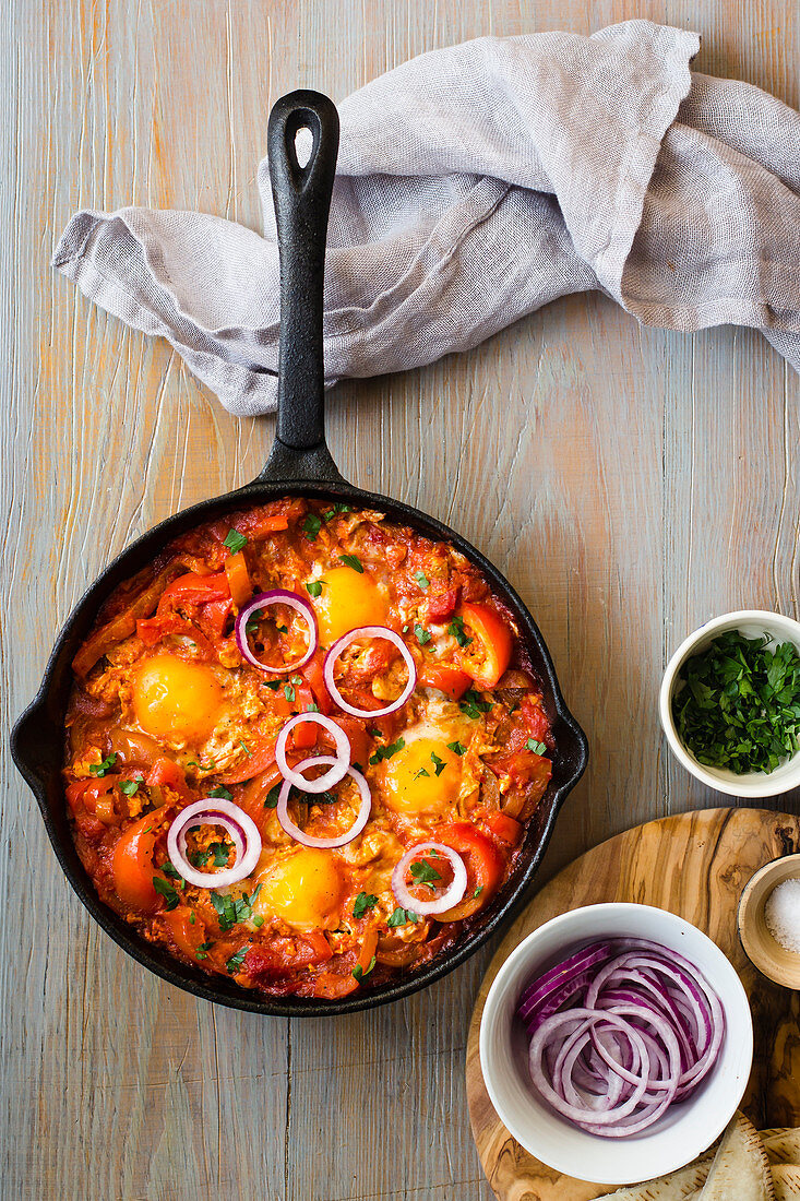 Shakshouka with peppers and tomatoes, chopped parley, rings of red onion and salt