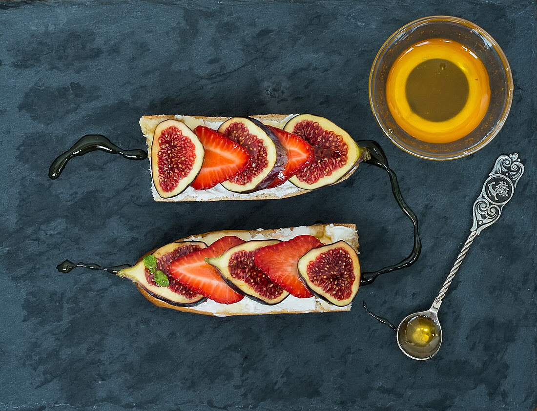 Fig and strawberry goat cheese sandwiches with honey on a dark stone surface
