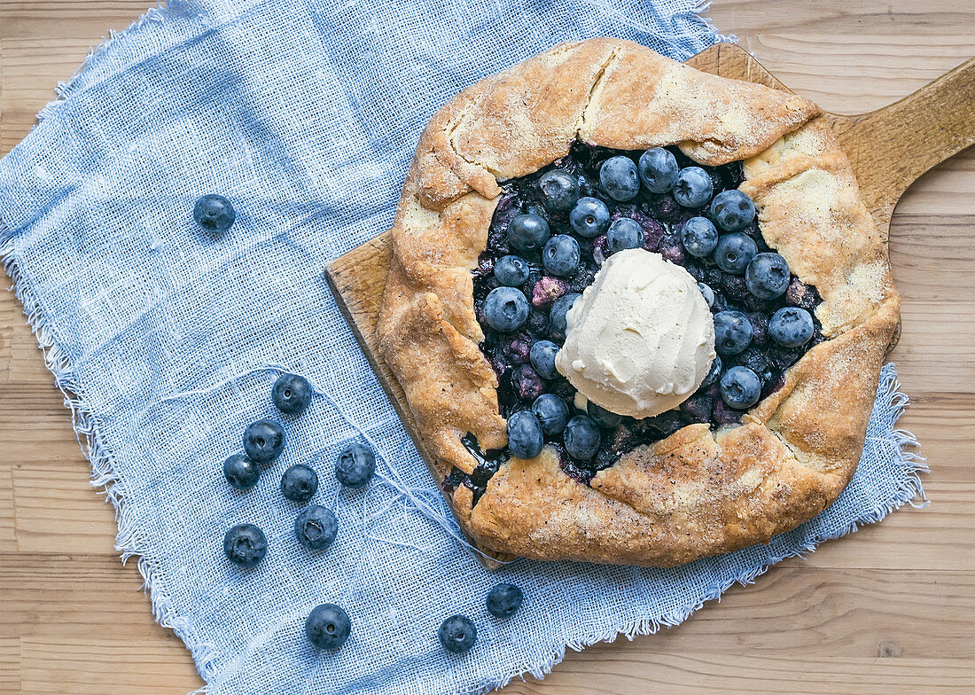 Rustic blueberry pie with ice-cream on a wooden board and white tissue