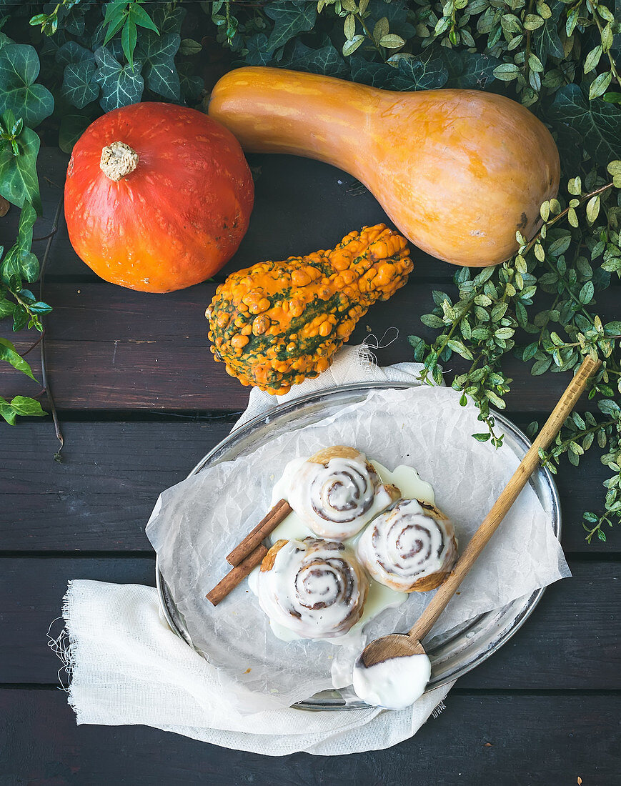 Cinnamon pumpkin buns with creamy cheese icing and ripe pumpkins over a dark wood background
