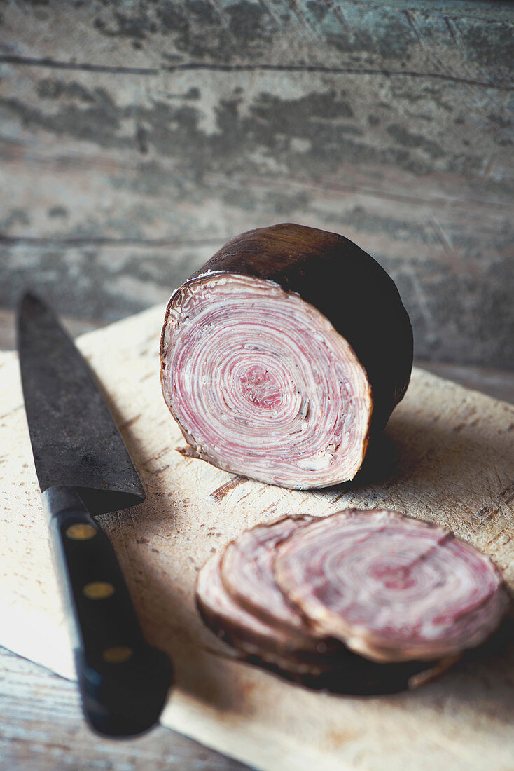 A a sliced French Andouille de Guéméné tripe sausage on a wooden board with a vintage Sabatier knife