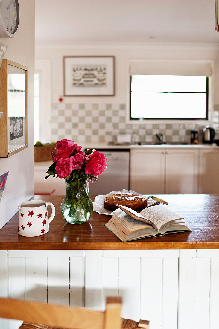 Vase of roses, open book and cake in country-house kitchen