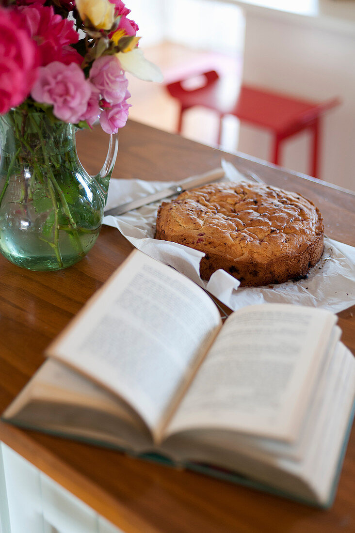 Open book, cake and vase of multicoloured roses on counter