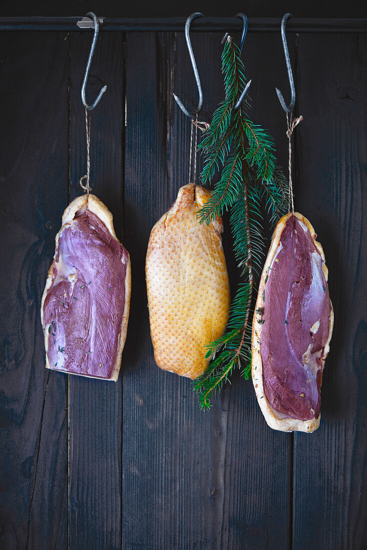 Three home smoked duck breasts suspended in a wooden smoker with a spruce branch