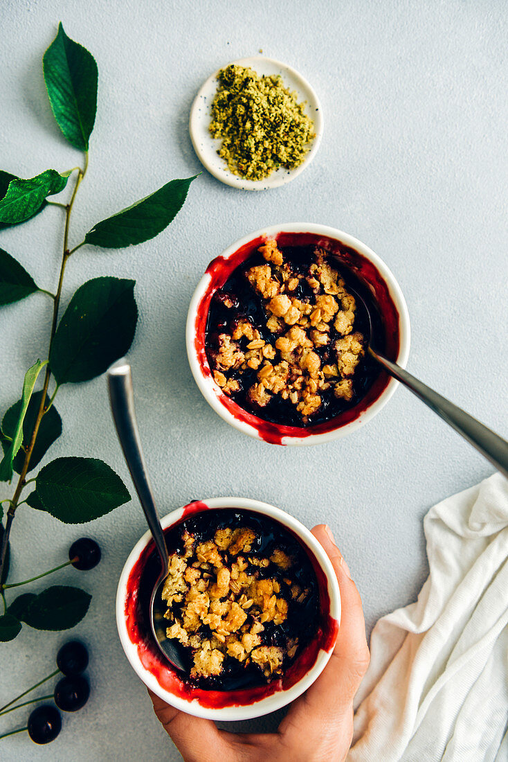 A woman holding cherry crisp with oats in a white ramekin with a spoon