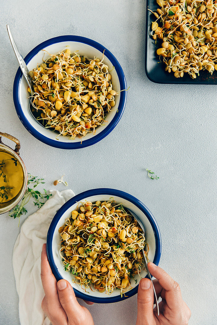 Person holding a a bowl of spicy sprouted lentils with corn on a grey background